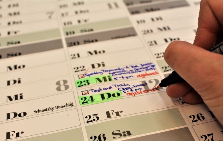 A hand is holding a pen and is writing event days for Cambridge Exams by Swiss Exams into a calendar. The Events take place on february first and second.