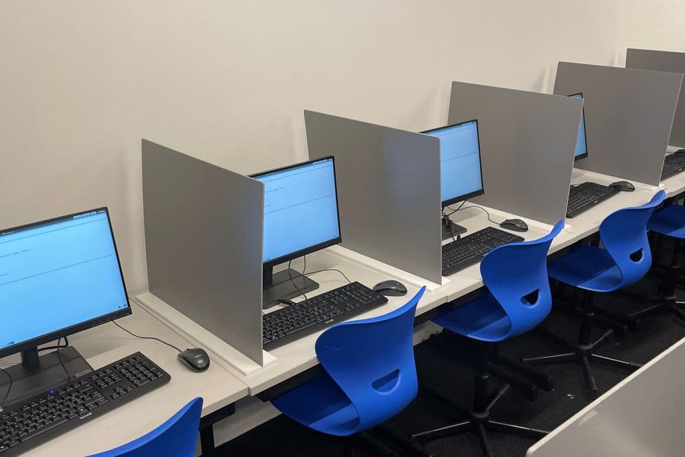 Vier blaue Stühle pro Arbeitsplatz mit einem Computer. Computer ist aufgestartet und zeigt die Homepage der Prüfung an.