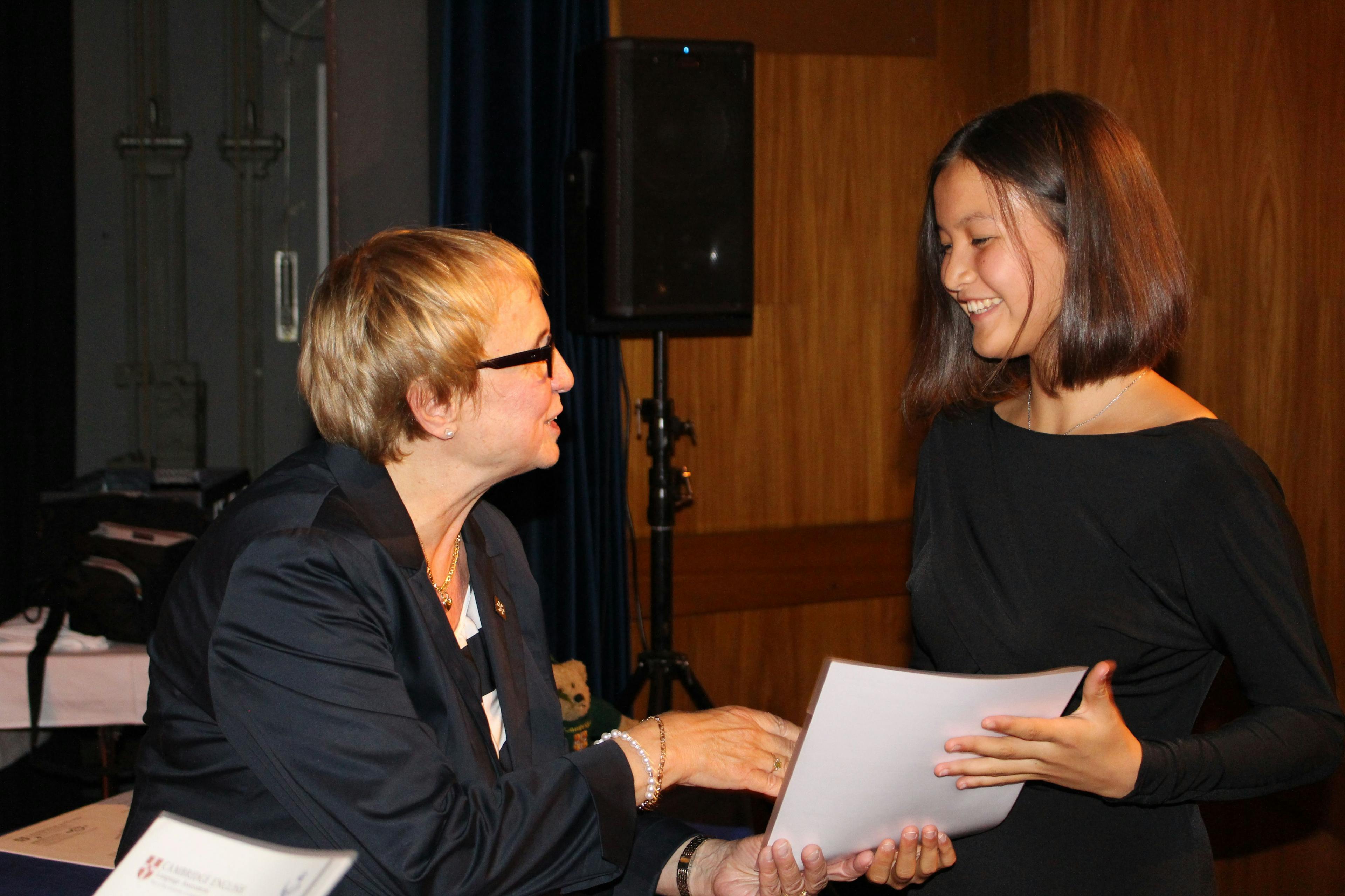 Swiss Exams former CEO Lori Kaithan hands out a language certificate to a student. They shake hands because the student passed the exam.
