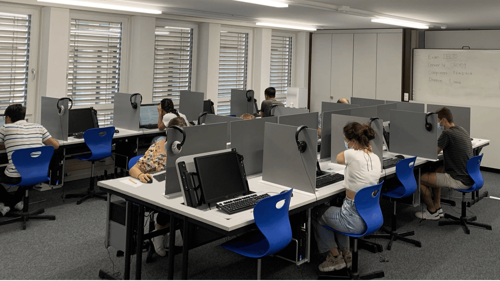 Students sitting on blue chairs in an computer-based exam room. They are taking an exam with Swiss Exams, the expert in exam management in Switzerland. 