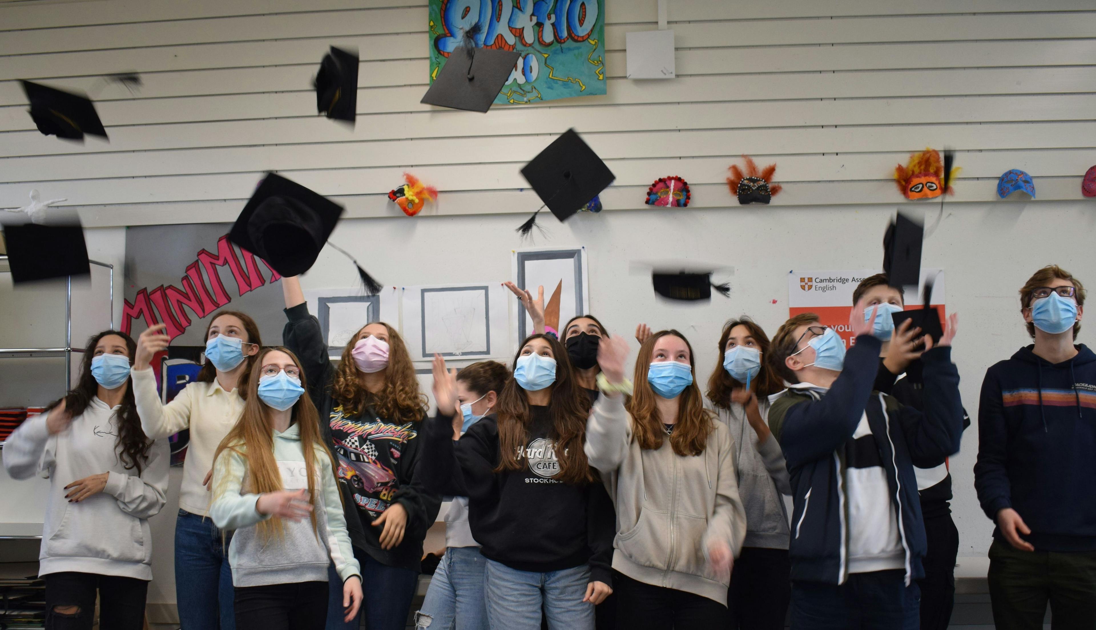 Students from the Sekundarschule have passed their Cambridge English Exam with distinction. They are in their classroom and throw black graduation hats.