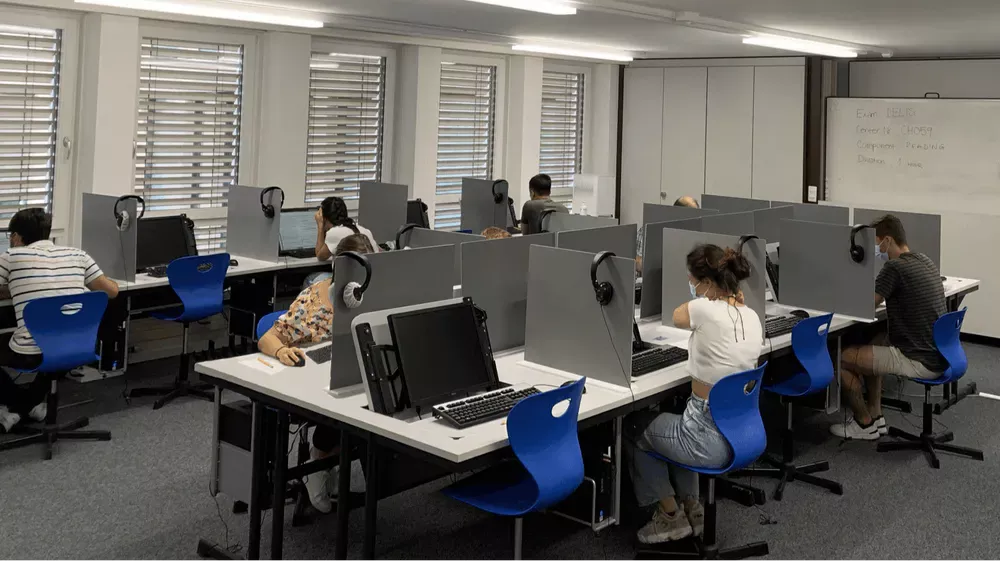 Students sitting on blue chairs in an computer-based exam room. They are taking an exam with Swiss Exams, the expert in exam management in Switzerland.
